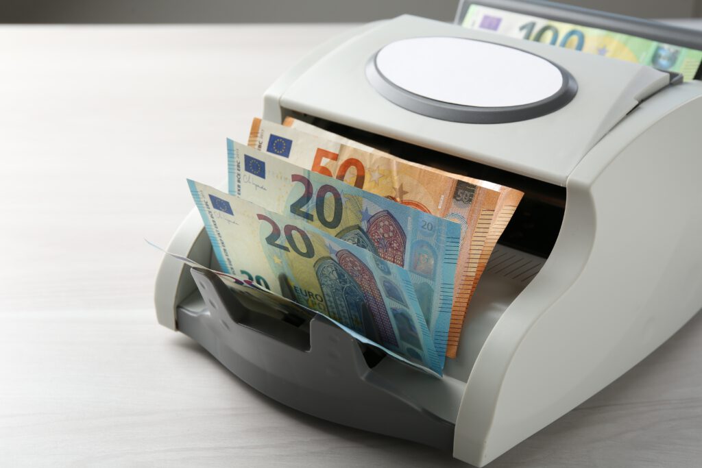 money counter machine with euro banknotes on white wooden table, closeup